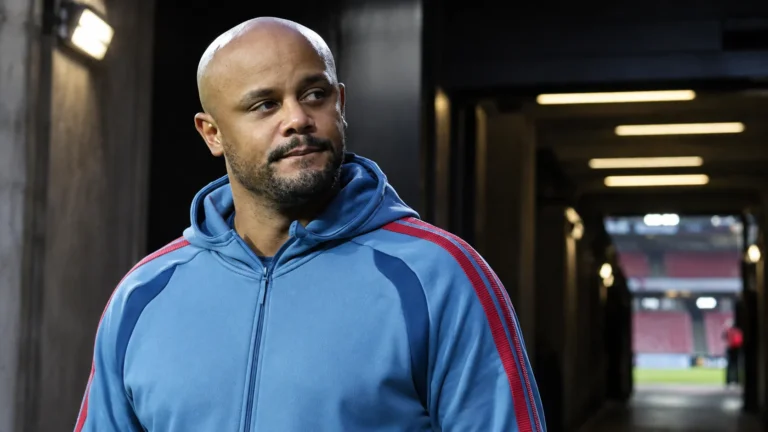 Vincent Kompany in een blauw sportjack bij de ingang van een voetbalstadion.