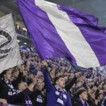 Collectieve paars-witte supporters op de tribune met grote vlaggen.