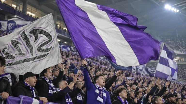 Collectieve paars-witte supporters op de tribune met grote vlaggen.