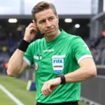 Een scheidsrechter in groen tenue voert voor de aftrap een controle uit op het veld.