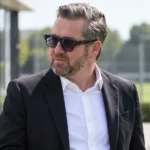 Een niet nader genoemde voetbalofficial in pak buiten een voetbalcomplex.