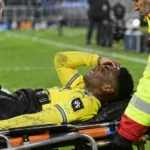Dylan Ourega krijgt verzorging naast het veld terwijl hij op een brancard ligt.