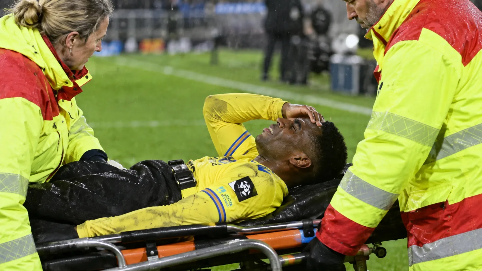 Dylan Ourega krijgt verzorging naast het veld terwijl hij op een brancard ligt.