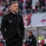 Een coach van RB Leipzig in zwarte kleding aan de zijlijn tijdens een wedstrijd.