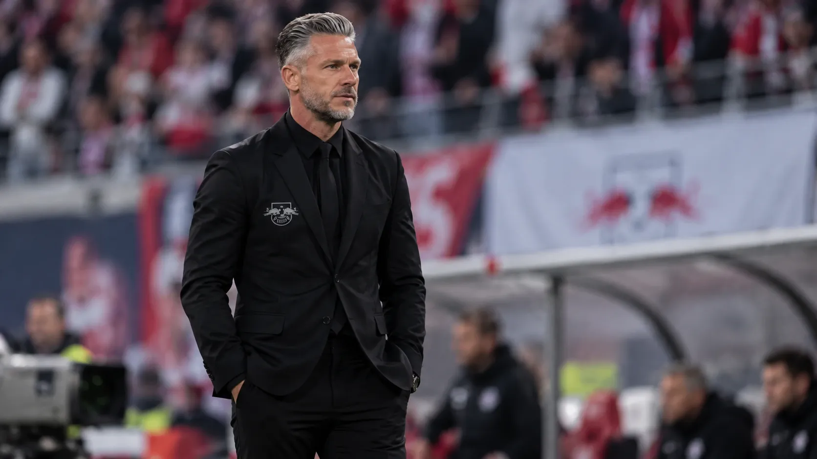 Een coach van RB Leipzig in zwarte kleding aan de zijlijn tijdens een wedstrijd.