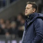 Michael Beale in een blauwe jas aan de zijlijn van een voetbalstadion.
