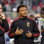 Drie Belgische voetballers in zwarte trainingsjassen praten naast het veld.