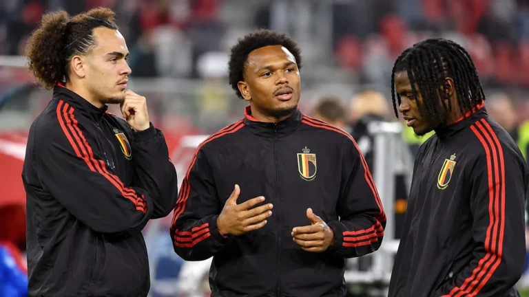 Drie Belgische voetballers in zwarte trainingsjassen praten naast het veld.