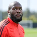 Romelu Lukaku in een rode trainingsjas aan de rand van een trainingsveld.