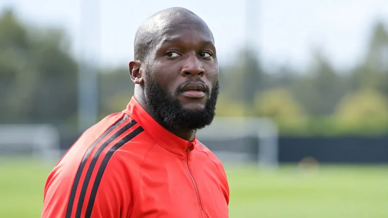 Romelu Lukaku in een rode trainingsjas aan de rand van een trainingsveld.