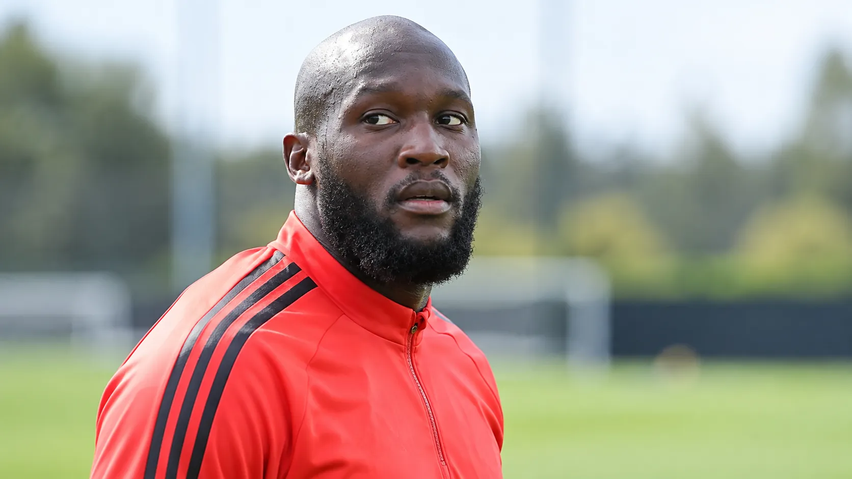Romelu Lukaku in een rode trainingsjas aan de rand van een trainingsveld.