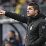 Een coach in donkere sportkleding die vanaf de zijlijn aanwijzingen geeft.