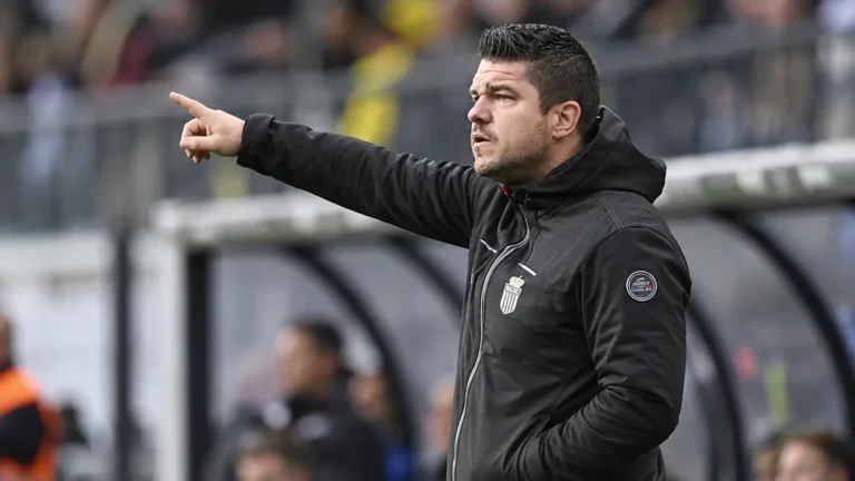 Een coach in donkere sportkleding die vanaf de zijlijn aanwijzingen geeft.
