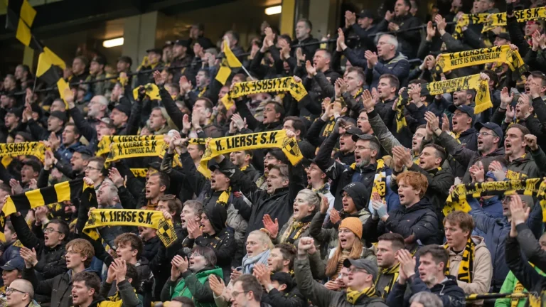 Een volle groep supporters met geel-zwarte sjaals op de tribune.