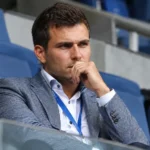 Een clubofficial in pak zit op een stadiontribune.