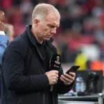 Paul Scholes kijkt op een smartphone aan een mediawerkplek in een voetbalstadion.
