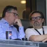 Twee niet-spelende clubvertegenwoordigers in een stadionloge tijdens een gesprek.