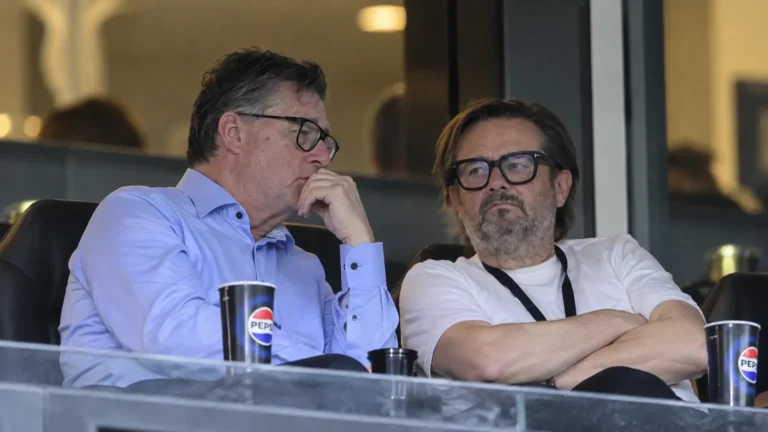 Twee niet-spelende clubvertegenwoordigers in een stadionloge tijdens een gesprek.