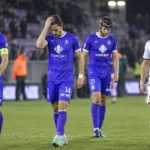 Spelers in paarse en witte tenues verlaten na een wedstrijd het veld.