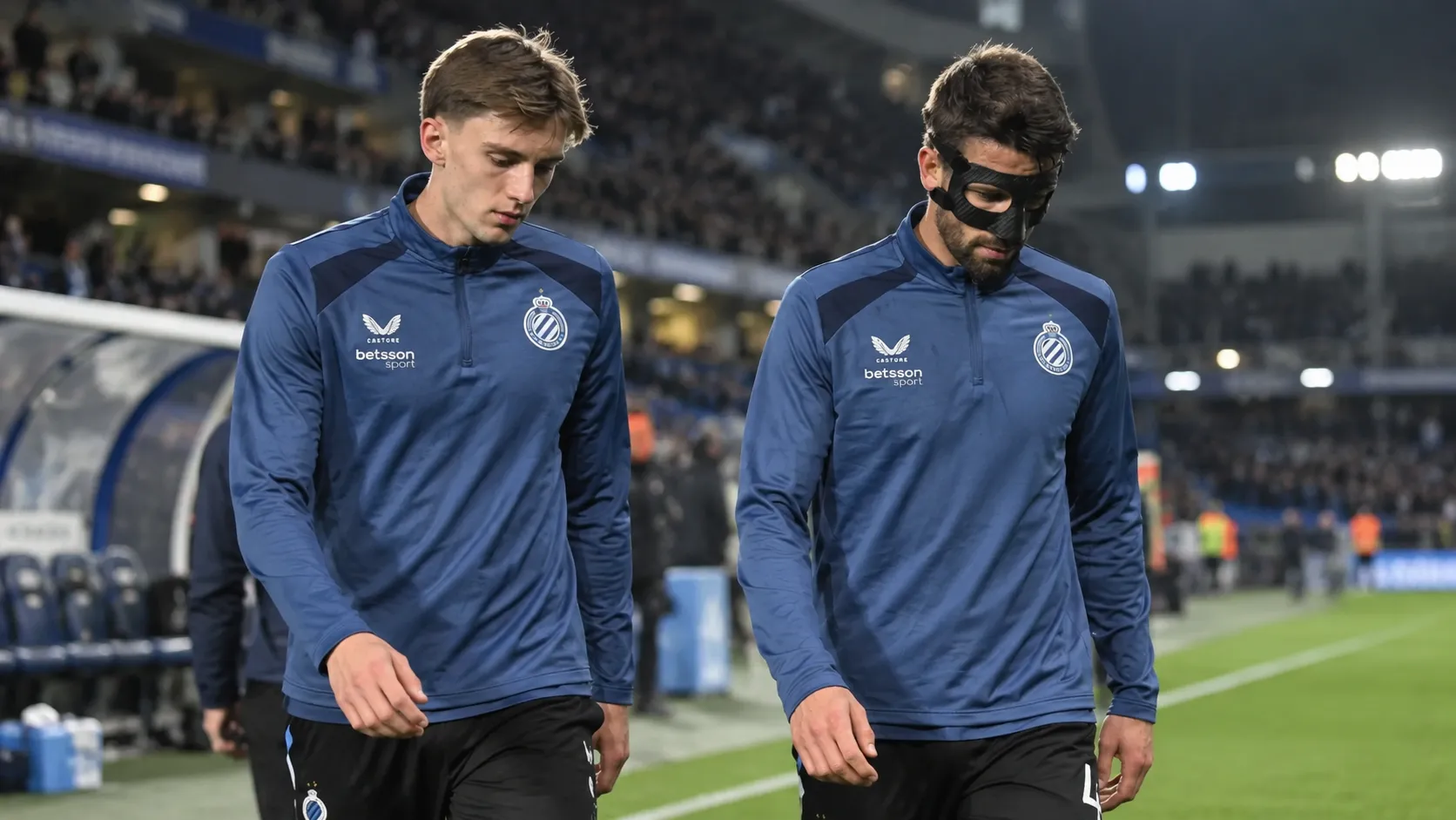 Twee spelers van Club Brugge lopen na een wedstrijd langs de zijlijn.