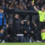 Een scheidsrechter toont een gele kaart aan een speler van Club Brugge naast de dug-out.