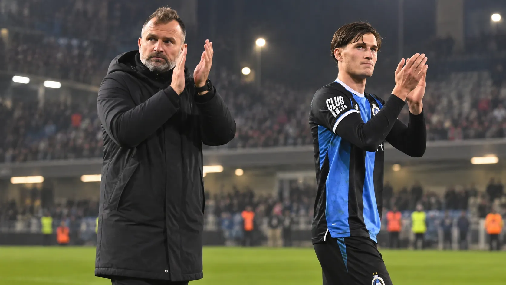 Een Club Brugge-trainer en speler applaudisseren na een wedstrijd in het stadion.