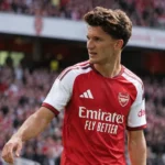 Een voetballer in een rood-wit Arsenal-shirt tijdens een wedstrijdmoment nabij de zijlijn.