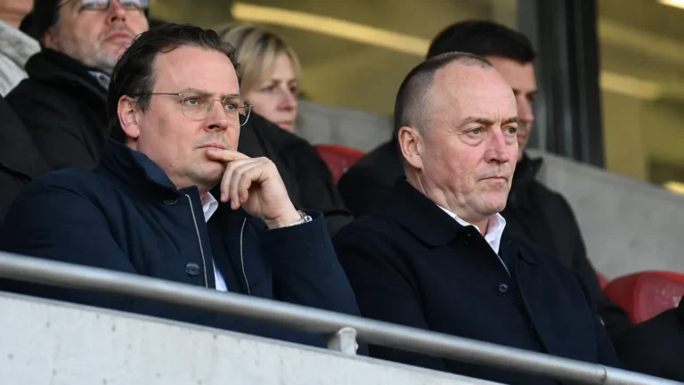 Niet-spelende clubvertegenwoordigers in donkere jassen op de tribune van de Bosuil.