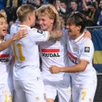 Een groep voetballers viert samen langs de zijlijn voor een supportersvak.