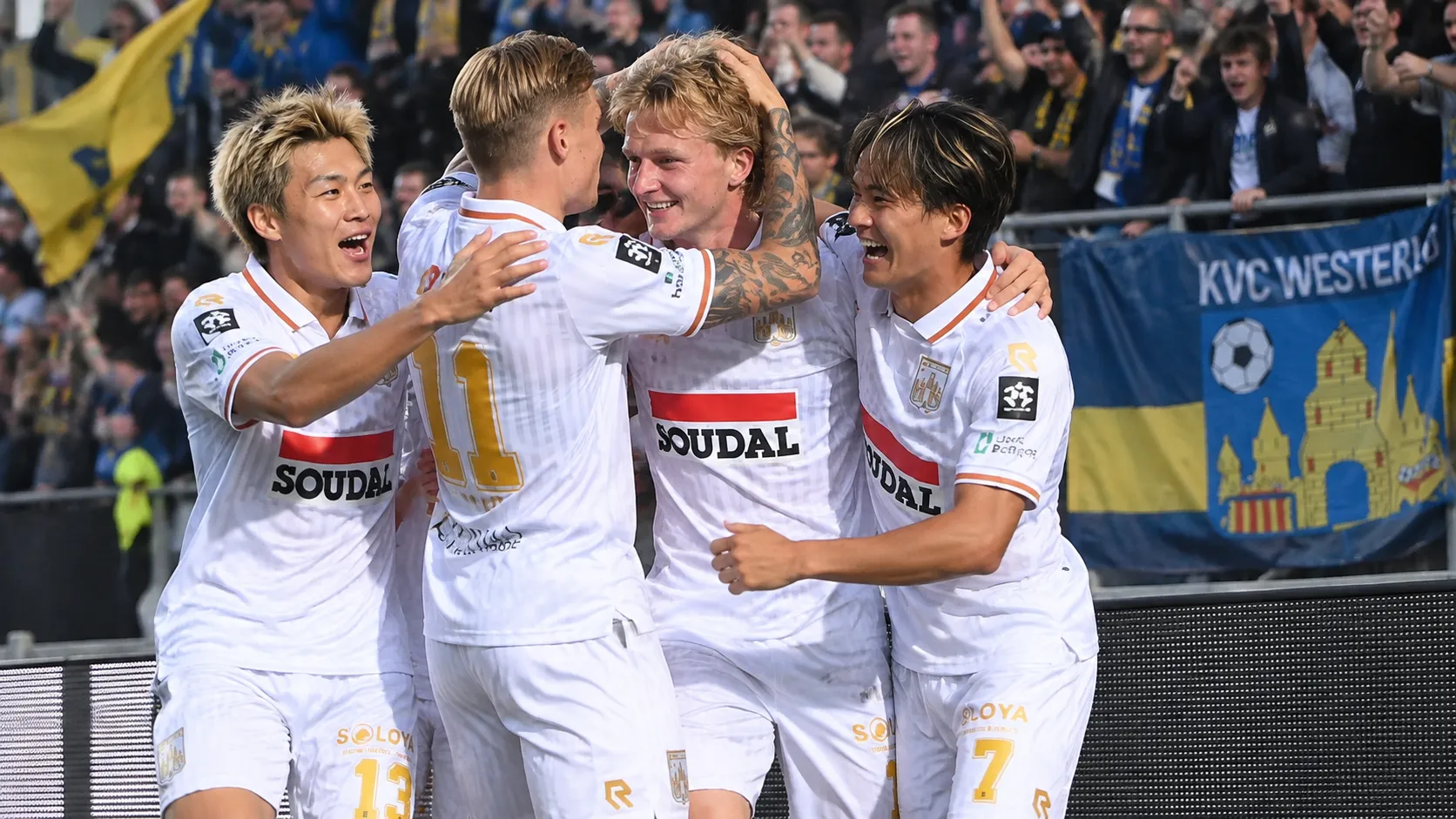 Een groep voetballers viert samen langs de zijlijn voor een supportersvak.