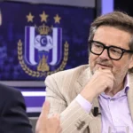 Marc Coucke spreekt in een televisiestudio met een subtiel RSC Anderlecht-embleem op een studiemonitor.