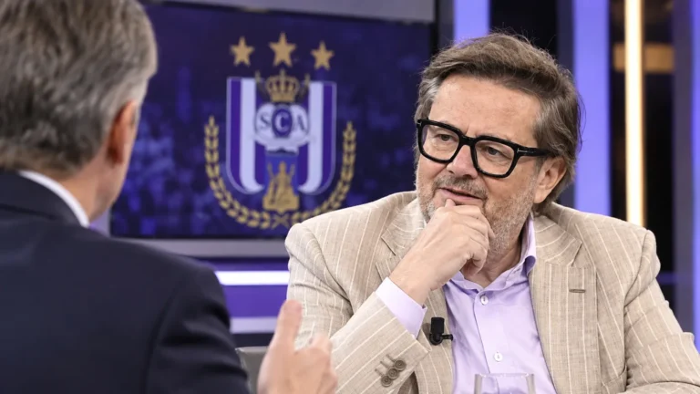 Marc Coucke spreekt in een televisiestudio met een subtiel RSC Anderlecht-embleem op een studiemonitor.