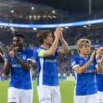 Een groep KRC Genk-spelers applaudisseert in de Cegeka Arena onder de verlichte LED-ring.