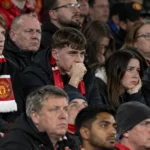 Een groep Manchester United-supporters met sjaals op de tribune van Old Trafford.