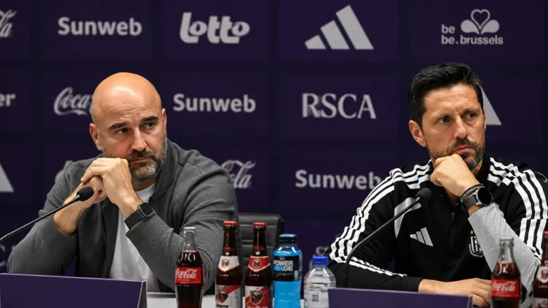 Twee deelnemers aan een persconferentie zitten achter een tafel met microfoons.