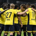 Een groep voetballers in geel-zwarte wedstrijdtenues verzamelt zich op het veld.