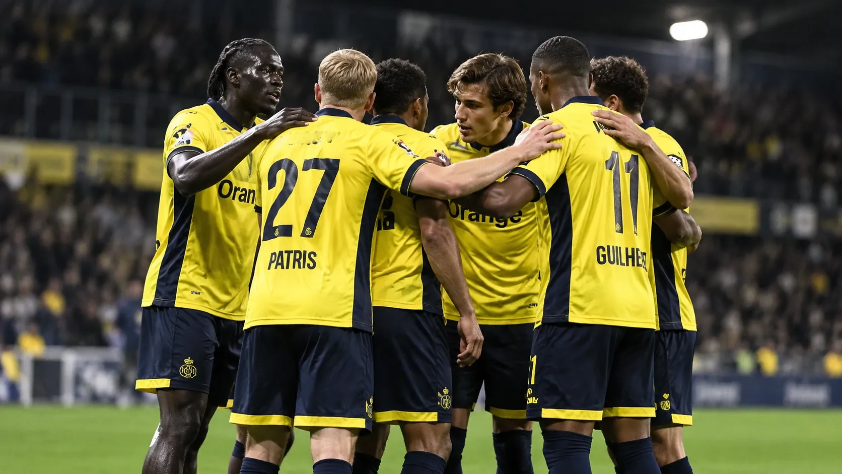 Een groep voetballers in geel-zwarte wedstrijdtenues verzamelt zich op het veld.