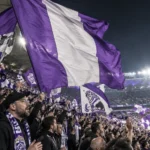Anderlecht-supporters zwaaien met paarse vlaggen in een volle tribune.
