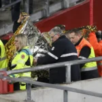 Een groep Standard-supporters applaudisseert in de tribune bij een medische interventie.