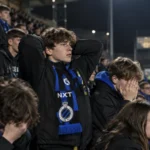 Collectieve Club NXT-supporters met blauw-zwarte sjaals in de tribune.