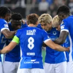 Een groep voetballers in blauwe shirts vormt een hechte huddle op het veld.