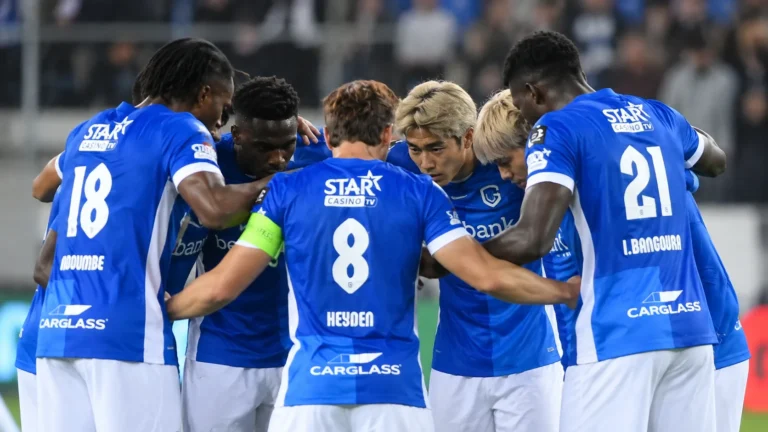 Een groep voetballers in blauwe shirts vormt een hechte huddle op het veld.