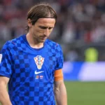 Een Kroatische speler in een blauw geruit nationaal shirt wandelt na de wedstrijd op het veld.
