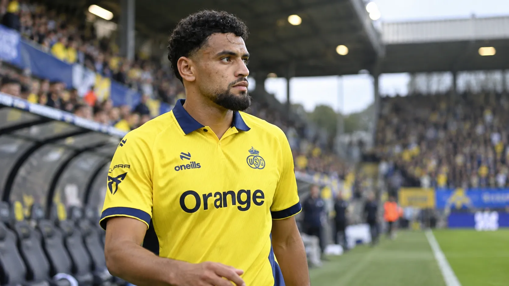 Adem Zorgane in het gele tenue van Union aan de rand van het veld.