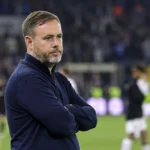 Michael Beale staat peinzend langs de zijlijn van een voetbalstadion.