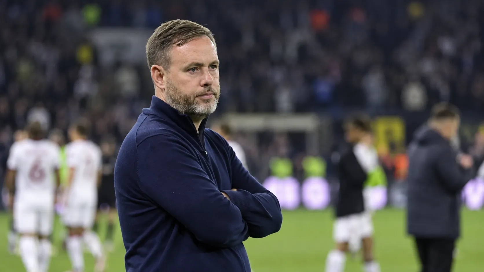 Michael Beale staat peinzend langs de zijlijn van een voetbalstadion.