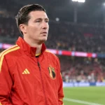 Hans Vanaken in een rode trainingsjas van België aan de zijlijn van een verlicht stadion.