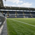 Leeg Jupiler Pro League-stadion met een competitiebord langs het veld.