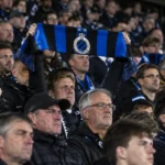 Een groep Club Brugge-supporters op de thuistribune met één omhooggehouden clubsjaal.