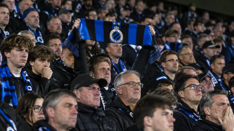 Een groep Club Brugge-supporters op de thuistribune met één omhooggehouden clubsjaal.